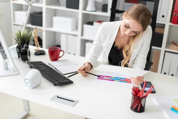 Een jong meisje zit aan de balie van de computer in het kantoor, houdt een potlood in haar hand en werken met documenten. — Stockfoto