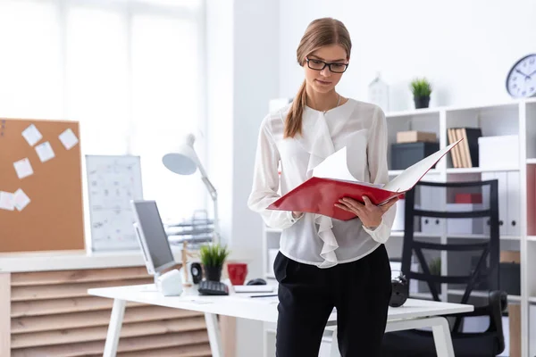 Een jong meisje staat in de buurt van een computerbureau en bladert door een map met documenten. — Stockfoto