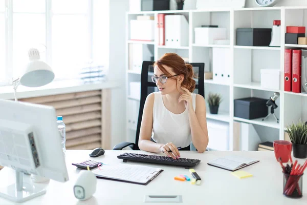 Bella ragazza in ufficio che lavora con i documenti, tenendo una penna in mano e guardando il monitor . — Foto Stock