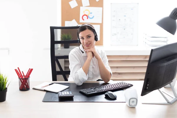 Een jong meisje in hoofdtelefoon met een microfoon zitten aan een tafel computer. — Stockfoto