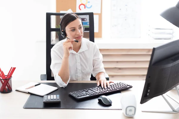 Een jong meisje in hoofdtelefoon met een microfoon zitten aan een tafel computer. — Stockfoto