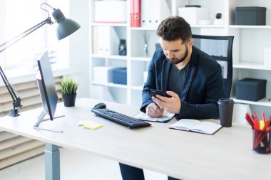 Genç adam bir bilgisayar danışma belgeleri, diyagramları ve telefon ile ofiste çalışır.