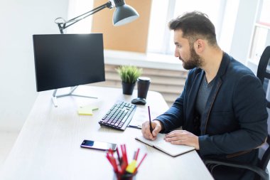 Genç adam bir bilgisayar danışma belgeleri, diyagramları ve telefon ile ofiste çalışır.