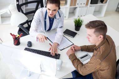 Doktor klavyede yazarak ve bilgisayarda Office hastaya sorunu açıklayan boynuna phonendoscope ile 