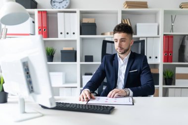 Genç bir adam ofiste bir tabloda yakın duran, telefonda konuşurken ve metin klavyede yazma.