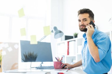 Zeki bir genç adam parlak bir ofisi telefon ile çalışır. 