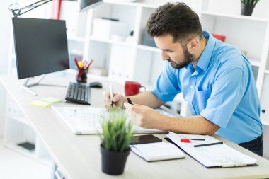 ofiste genç adam bir masada oturur ve belgeleriyle çalışır.