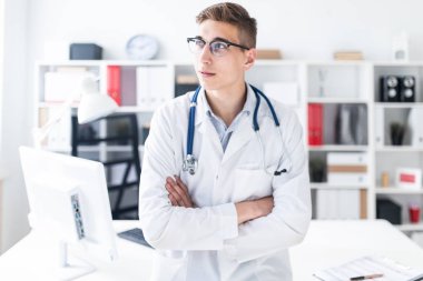 Önlük üzerinde boyun ayakta stetoskop ile genç doktor ofisinde çapraz kolları olan