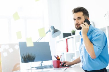 Zeki bir genç adam parlak bir ofisi telefon ile çalışır. 