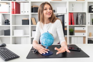 bilgisayarda ofis masasında oturan ve bir küre tutan genç iş kadını.