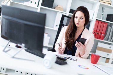 bir bilgisayar başında oturan ve bir telefon tutarak genç iş kadını 