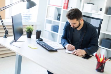 Genç adam bir bilgisayar danışma belgeleri, diyagramları ve telefon ile ofiste çalışır.