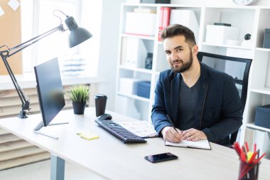 Genç adam bir bilgisayar danışma belgeleri, diyagramları ve telefon ile ofiste çalışır.