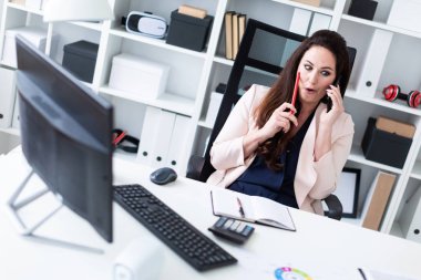 bir bilgisayar başında oturan ve bir telefon tutarak genç iş kadını 