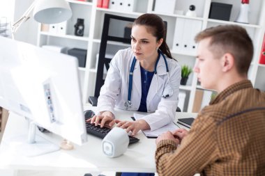 Doktor klavyede yazarak ve bilgisayarda Office hastaya sorunu açıklayan boynuna phonendoscope ile 