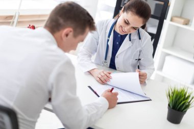 genç hasta doktor masada oturan ve Office sağlık sigortası belgelerin imzalanması