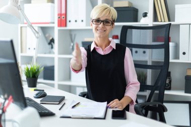 Genç bir kız ofiste bir masada oturur ve elini uzanır.