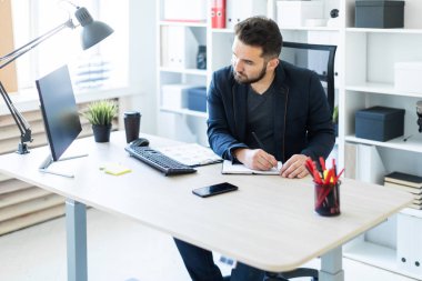 Genç adam bir bilgisayar danışma belgeleri, diyagramları ve telefon ile ofiste çalışır.