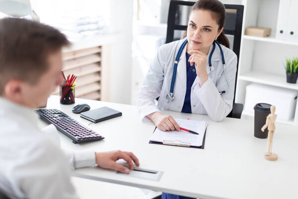 beautiful young doctor in white lab coat listening carefully to male patient in office 