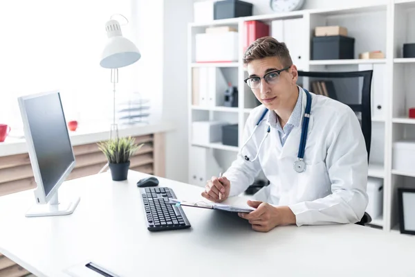 Jovem Médico Segurando Prancheta Lendo Documentos Enquanto Sentado Mesa Escritório — Fotografia de Stock