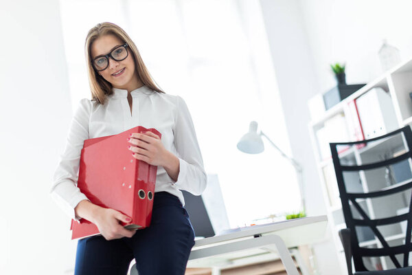 young girl stands near a computer Desk and holds a folders with documents
