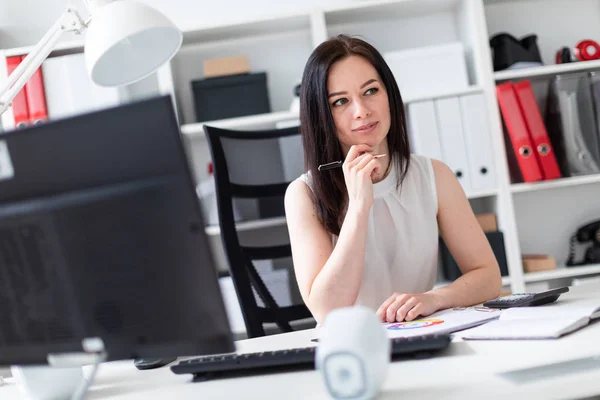 En ung flicka sitter på kontoret på en dator skrivbord och arbeta med dokument och en miniräknare. — Stockfoto