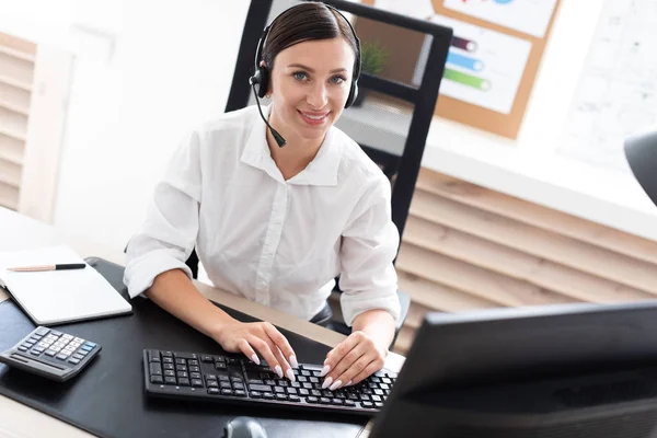 Una joven en auriculares con un micrófono sentado en una mesa de ordenador . — Foto de Stock