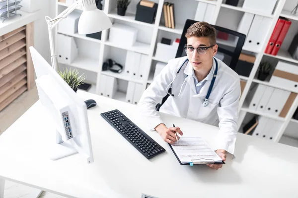 Giovane Medico Possesso Bordo Ritaglio Lettura Documenti Mentre Seduto Alla — Foto Stock