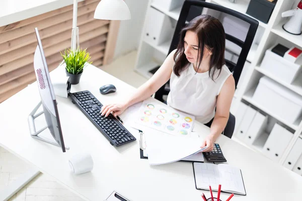 Una joven sentada en la oficina en un escritorio de computadora y trabajando con documentos y una calculadora . — Foto de Stock
