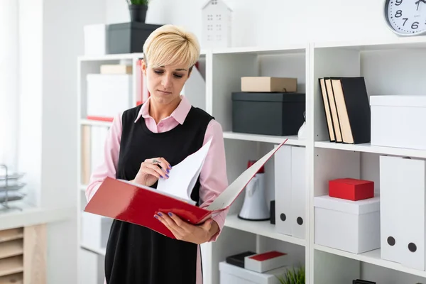 young girl stands in the office with a red folder in her hands.