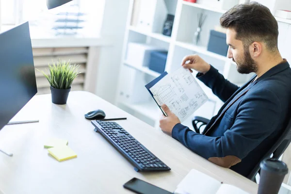 El joven trabaja en la oficina en una computadora Escritorio con documentos, diagramas y teléfono . — Foto de Stock