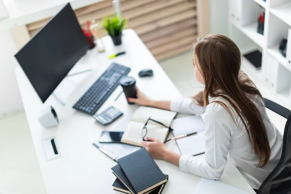 Een jong meisje ging zitten op de tabel en werkt met een computer, documenten en calculator — Stockfoto