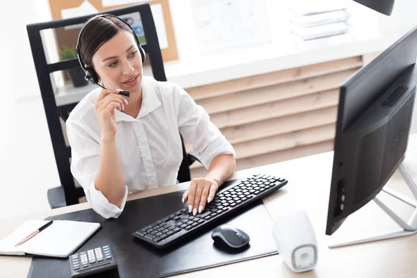 Una joven en auriculares con un micrófono sentado en una mesa de ordenador . — Foto de Stock