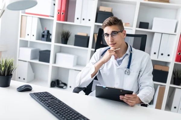 Jovem Médico Segurando Prancheta Lendo Documentos Enquanto Sentado Mesa Escritório — Fotografia de Stock