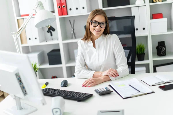 Een jong meisje ging zitten op de tabel en werkt met een computer, documenten en calculator — Stockfoto