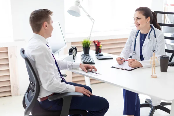 smiling doctor discussing with patient while while sitting at table in office