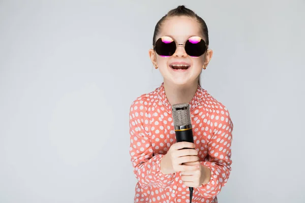 Meisje op een grijze achtergrond-zingen in de microfoon. — Stockfoto