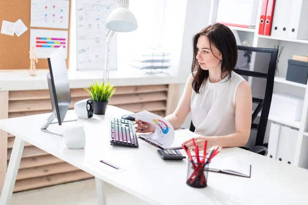 En ung flicka sitter på kontoret på en dator skrivbord och arbeta med dokument och en miniräknare. — Stockfoto