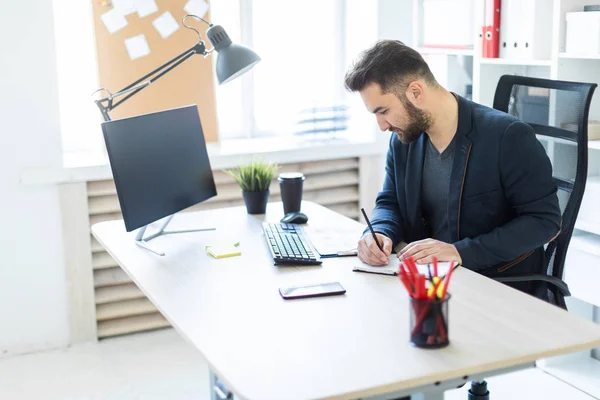 Der junge Mann arbeitet im Büro an einem Computertisch mit Dokumenten, Diagrammen und Telefon. — Stockfoto