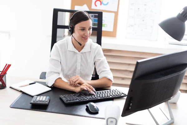 Una joven en auriculares con un micrófono sentado en una mesa de ordenador . — Foto de Stock