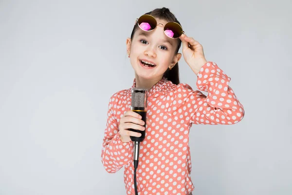 Meisje op een grijze achtergrond-zingen in de microfoon. — Stockfoto