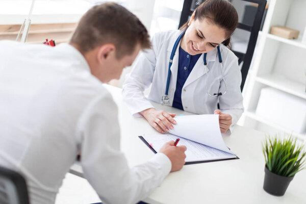 young patient sitting with doctor at table and signing health insurance documents in office