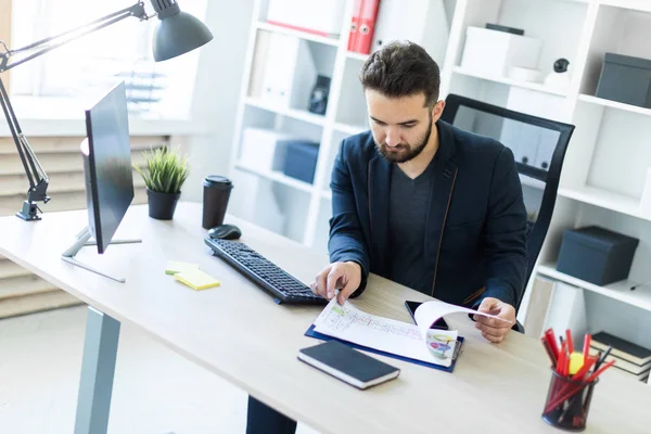 El joven trabaja en la oficina en una computadora Escritorio con documentos, diagramas y teléfono . — Foto de Stock