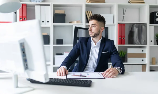 Un joven está de pie cerca de una mesa en la oficina, hablando por teléfono y escribiendo texto en el teclado . — Foto de Stock