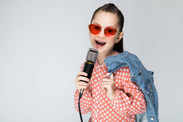 Девушка на сером фоне поет в микрофон
.