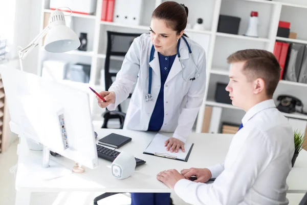 年轻的医生在实验室外套指向电脑屏幕和解释问题在办公室的患者 — 图库照片