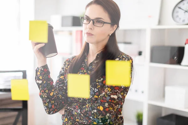 young economist with coffee cup in hand thoughtfully looking at board with yellow stickers in office