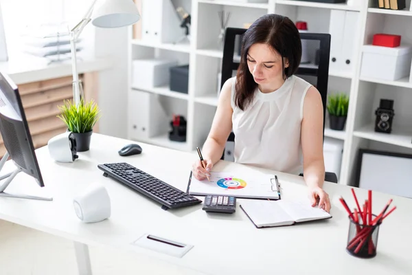 Una joven sentada en la oficina en un escritorio de computadora y trabajando con documentos y una calculadora . — Foto de Stock