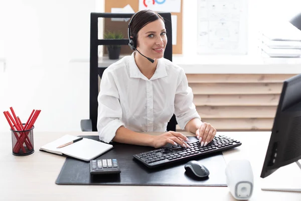 Una joven en auriculares con un micrófono sentado en una mesa de ordenador . — Foto de Stock