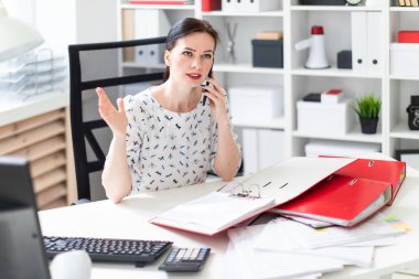 Office belgeleriyle çalışma ve telefonda konuşurken masası, bilgisayar başında oturan bir genç kız.